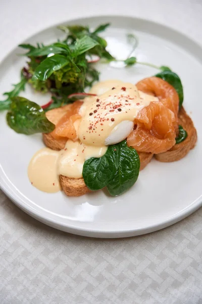 Top-view restaurant serving of smoked salmon eggs benedict on white plate, restaurant brunch