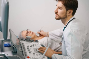 Uzist yaşlı bir bayana tiroit bezini ultrasonla muayene ediyor. Doktor modern ekipman kullanıyor.