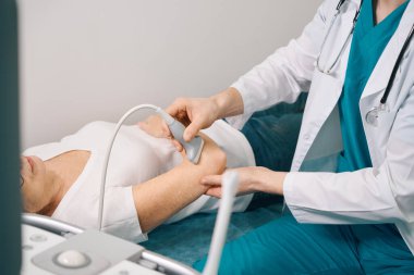 Yaşlı bir kadın ultrason makinesinde eklem inceliyor, doktor modern ekipman kullanıyor.