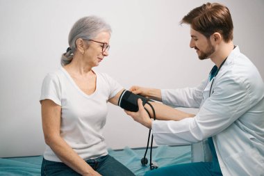 Genç doktor hastaya kan basıncını ölçüyor, doktor bir tonometre ve stetoskop kullanıyor.