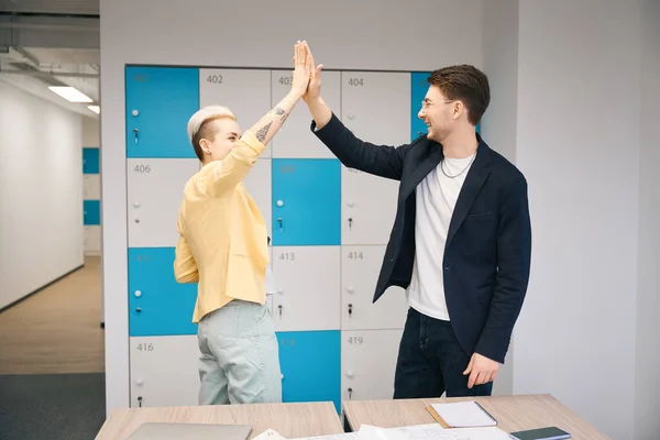 Creative team giving high five to each other after successfuly completed job in coworking space with storage cells, teamwork
