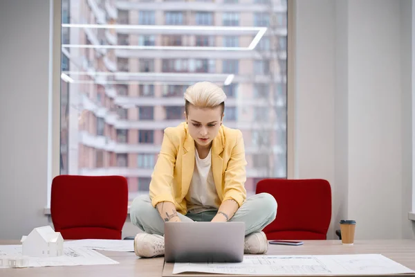 集中女性作業机の上に座ってノートパソコンで作業 より良いインスピレーションのための居心地の良い位置を探しています — ストック写真