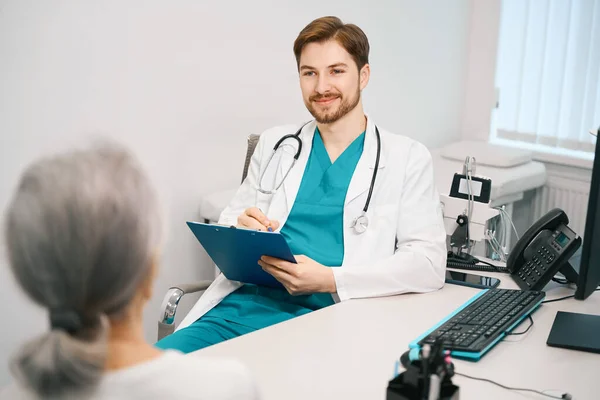 Pleasant Young Doctor Communicates Elderly Lady Therapy Room Writes Patients — Stock Photo, Image