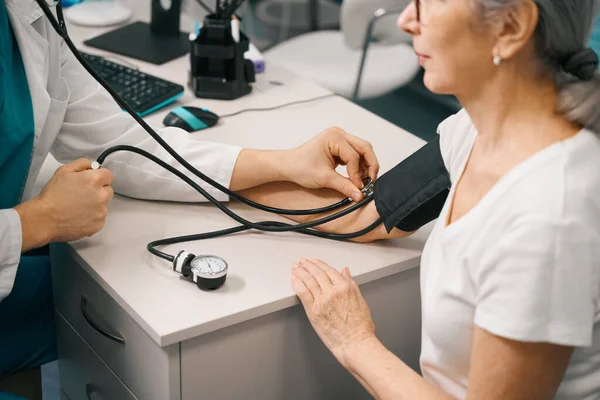 セラピストは年金受給者の血圧を測定し 医師はメートル法と聴診器を使用します — ストック写真