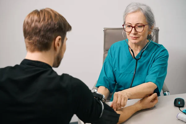 注意观察的女性治疗师测量年轻患者的血压 穿便服的男性 — 图库照片