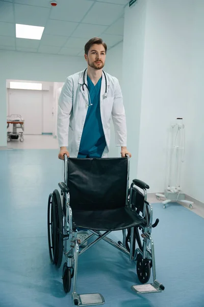 Médico Barbudo Carrega Uma Cadeira Rodas Longo Corredor Hospital Tem — Fotografia de Stock