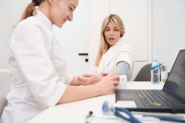 Gülümseyen kadın doktor, tonometresi olan bir hastaya kan basıncını ölçüyor, kadınlar teşhis bölümünde.