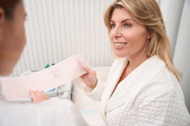 Teşhis departmanının çalışanı bir hastaya danışır. Ellerinde EKG sonuçları vardır.