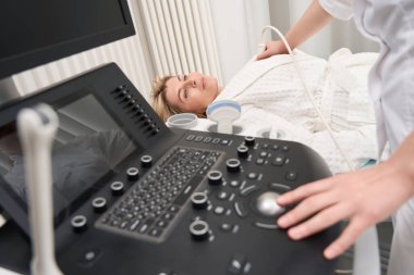 Ultrason uzmanı, departmandaki bornozlu, modern ekipmanlı bir bayana kalbin ultrasonunu yapıyor.