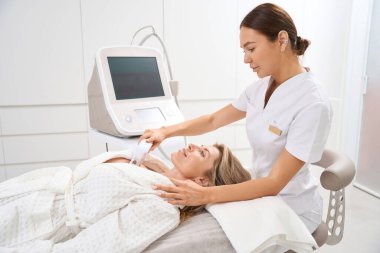 Güzellik uzmanı, hastanın başında oturur. Uzman, dekolte bölgesini kaldırır.