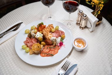 Lüks restoranda beyaz masa örtüsü üzerine şarap bardaklarıyla servis edilen farklı lezzetteki aperatiflerle dolu bir tabak.