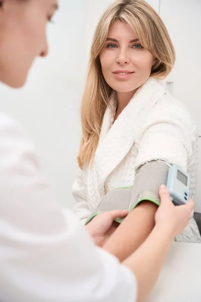 女医生用体能计测量病人的血压 而妇女则在诊断部门 — 图库照片
