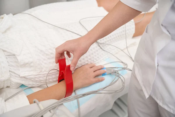 医学中心的女员工将传感器装在病人的手上进行心电图研究 病人躺在沙发上 — 图库照片