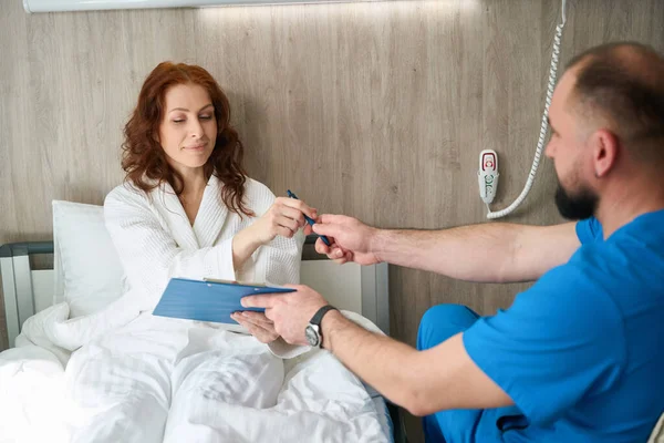 Male Doctor Giving Pen Clipboard Attractive Female Robe Medical Center — Stock Photo, Image