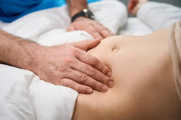 ベッドの上で病気の女性の腹部を調べる医師の手に近いビュー — ストック写真