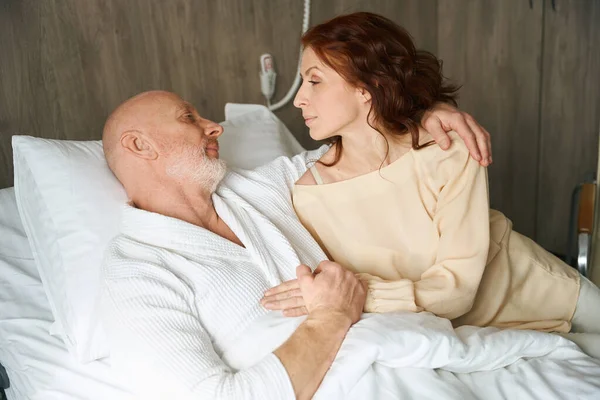 在现代医院的病房里 一对白种人夫妇躺在舒适的床上互相照料 — 图库照片
