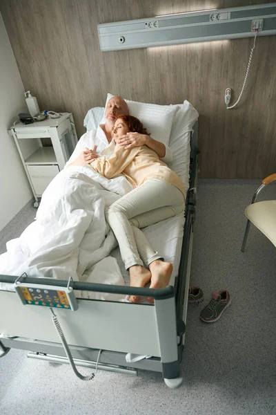 美丽的女人和她的丈夫在医疗中心躺在现代化的病床上互相扶持 — 图库照片