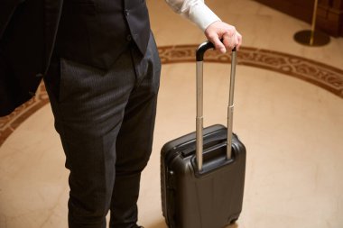 Otel lobisinde elinde siyah bavul olan bir adamın kesilmiş fotoğrafı.
