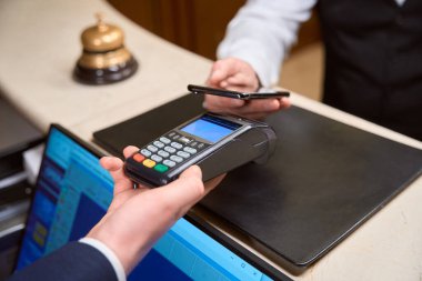 Yöneticinin kredi kartı okuyucusunu elinde tutarken, erkek müşterinin otel resepsiyonunda akıllı telefondan ulaşılamaz ödemeler yapmasını kapatın.