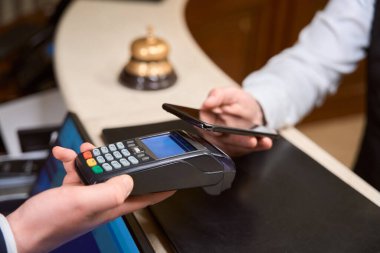 Otel resepsiyonunda kredi kartı okuyucu tutarken NFC teknolojisiyle ödeme yapan adama yakın çekim.