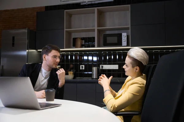 机の上のノートパソコンと居心地の良いオフィスに座っているプロジェクト計画を議論する2人の同僚 キッチンとのコワーキングスペース — ストック写真