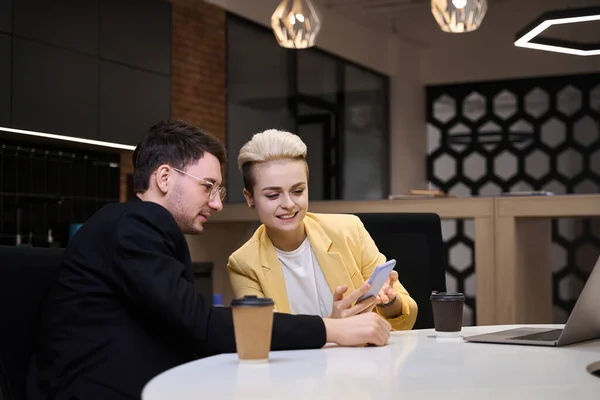 スマートフォンから男性パートナーへのスタートアップのアイデアを披露する笑顔の女性がオフィスで休憩中 — ストック写真