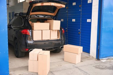 SUV karton kutularla dolu bir depoda açık bagajda ve arabanın yanında.