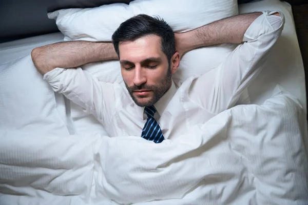Man, without undressing, fell asleep in office clothes, in a comfortable bed, he lies on a soft pillow
