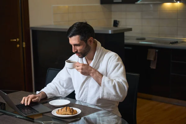 男人在厨房和饭厅里 坐在笔记本电脑前 喝着早茶 — 图库照片