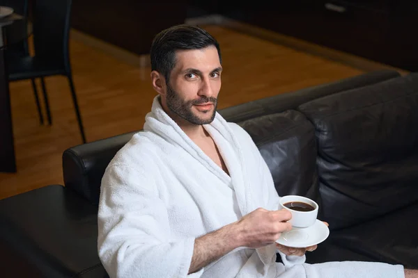 Middle-aged hotel guest enjoys a cup of morning coffee, a man sits on a comfortable leather sofa