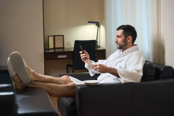 穿着浴衣的宾馆客人坐在一个有咖啡的休闲区 他通过手机与客人交流 — 图库照片