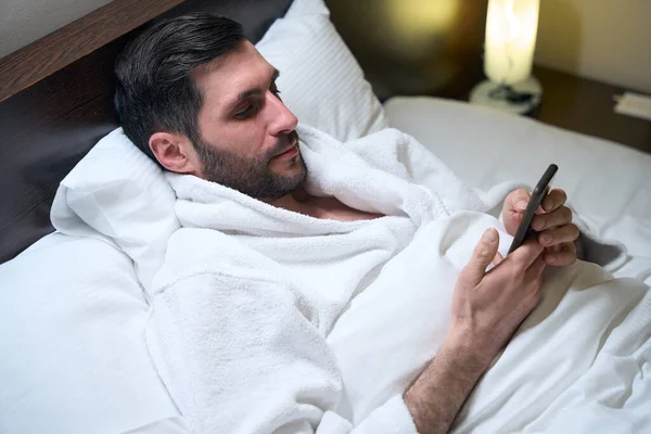 Nieogolony Mężczyzna Spoczywa Łóżku Miękkich Poduszkach Telefon Komórkowy Rękach — Zdjęcie stockowe