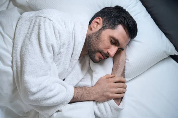 疲れた中年男性は柔らかい枕の上でベッドで眠り 彼は彼の側に横たわっています — ストック写真