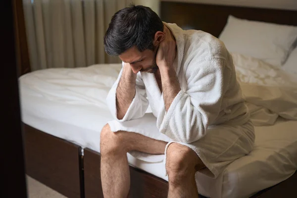Przygnębiony Mężczyzna Siedzi Dużym Łóżku Pokoju Hotelowym Nosi Wygodny Szlafrok — Zdjęcie stockowe