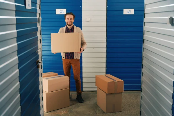 ハッピー男は大きな段ボール箱を保持し 多くのボックスと倉庫に立っている — ストック写真