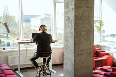 Ofiste pencerede otururken dizüstü bilgisayarla çalışan sorumlu erkek çalışanın arka planı