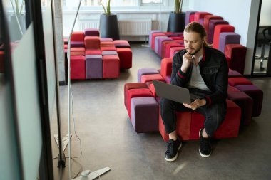 Kapalı mekanda bilgisayarla iş ödevi yaparken şık saç kesimi olan yakışıklı bir adam.