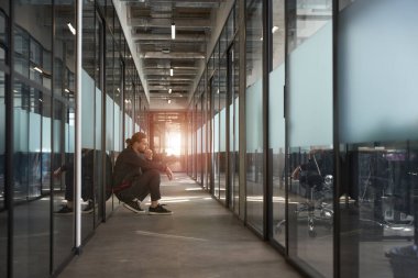 Ofis koridorunda otururken düşüncelere dalmış yakışıklı bir adam.