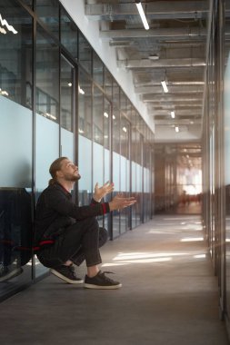 Şık saç kesimi olan şık bir erkek ofis koridorunda poposunun üzerinde otururken yukarı bakıyor.