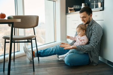 Sevgi dolu genç baba küçük kızıyla köfte oynuyor, yakınlardaki masada çeşitli sebzeler var.