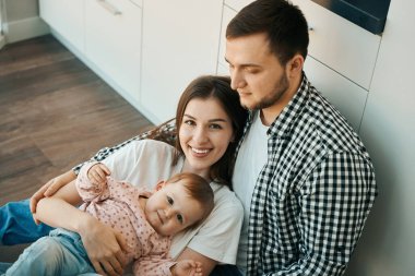 Neşeli anne ve bebek, mutfakta babasının kollarında oturuyor. Uzaktan kumandayla ailenle iletişim kuruyorsun.