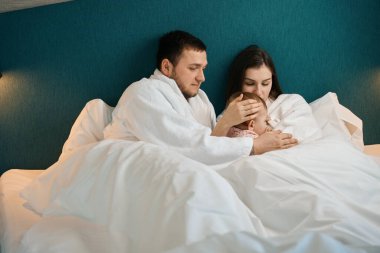 Genç anne kızını emziriyor, sevgi dolu baba da kızlarını kucaklıyor.