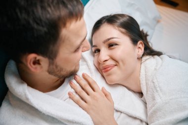 Güzel kadın kocasına sevgiyle bakar. Çift büyük bir yatağın altında güneşlenir.