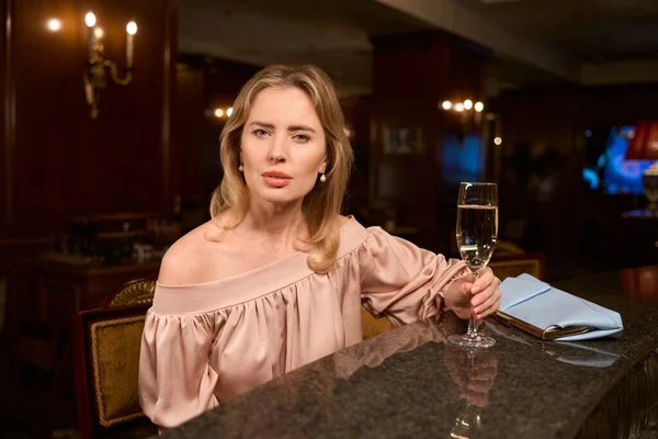 身着晚礼服的成年女性 喝着一杯葡萄酒 在酒吧的餐桌旁等着同事 — 图库照片