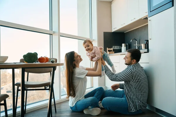 幸せな両親は家で小さな子供と遊ぶ 家族は台所の床に位置しています — ストック写真