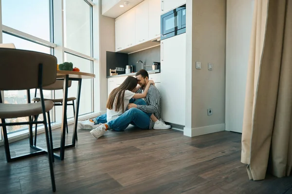 Laughing Young Spouses Sit Embracing Floor Kitchen Located View Window — Stock Photo, Image