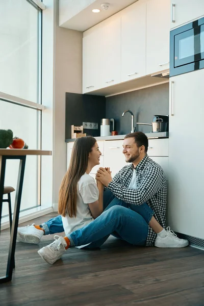 Laughing Young Spouses Sit Embracing Floor Kitchen Tenderly Hold Hands — Stock Photo, Image