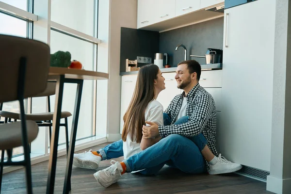 快乐的男人和女人正坐在厨房的地板上拥抱 厨房桌上有蔬菜 — 图库照片