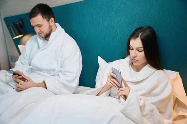 남자와 여자는 가정복을 부드러운 침대에 전화를 있습니다 — 스톡 사진