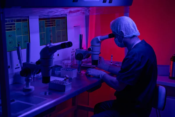 从事基因研究 医疗保健和医药的生物流产工作者 带着显微镜 数字显示器和微处理器坐在他的工作场所 — 图库照片